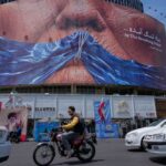 Vehicles drive past a billboard with graphic showing Strait of Hormuz and sewn lips of U.S. President Donald Trump in a square in downtown Tehran, Iran, Saturday, May 2, 2026. (AP Photo/Vahid Salemi)