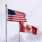 In this photo taken Sunday, May 17, 2020, U.S. and Canadian flags fly atop the Peace Arch at Peace Arch Historical State Park on the border with Canada, where people can walk freely between the two countries at an otherwise closed border, in Blaine, Wash. Canada and the U.S. have agreed to extend their agreement to keep the border closed to non-essential travel to June 21 during the coronavirus pandemic. The restrictions were announced on March 18, were extended in April and now extended by another 30 days. (AP Photo/Elaine Thompson)