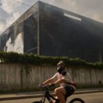 A local resident wears a gas mask as he rides a bicycle past a partially destroyed warehouse after a Russian drone attack in Brovary on the outskirts of Kyiv, Ukraine, Friday, Sept. 4, 2026. (AP Photo/Francisco Seco)
